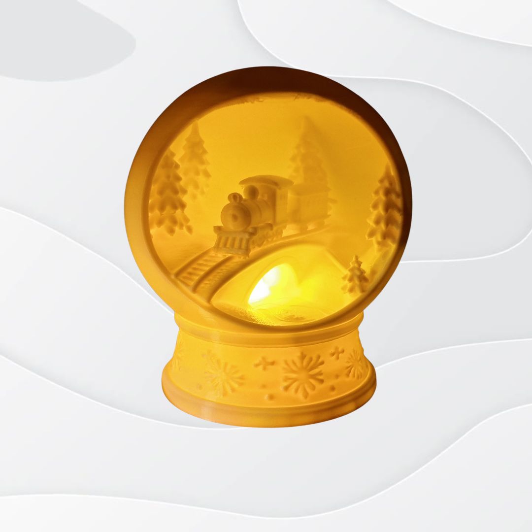 The 3D Printed Christmas Train Glow Dome is a ceramic lamp shaped like a snow globe, with a festive train and trees inside. It casts a warm LED light, features snowflake patterns on the base, and makes perfect holiday table decor.